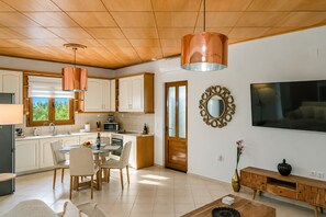 A modern kitchen with white cabinets, a dining area with a glass table, and a living room with a TV and decorative mirror. - Villa Avra - With Private Pool (Rethymno)