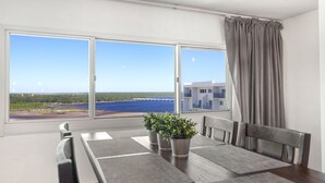 Uma varanda com mesa e cadeiras, um vaso de planta e vista para a água e edifícios.