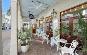 A covered outdoor seating area with white chairs and tables, potted plants, and a sign for 'The Salty Bottle.'