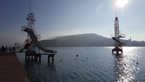 A water slide structure extending into a calm lake with a distant mountain and a church silhouette.