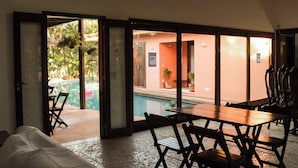 Um espaço de refeições interno com vista para uma piscina ao ar livre e um edifício com paredes alaranjadas.