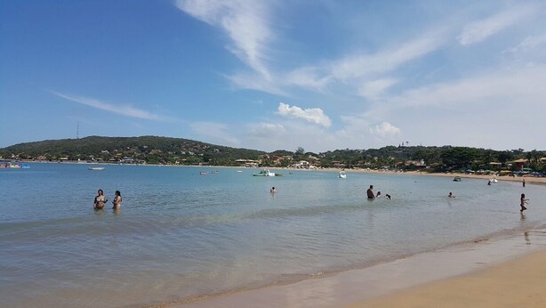 Uma praia com águas cristalinas, pessoas nadando e barcos.