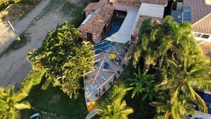 Vista aérea de uma propriedade com piscina, cercada por vegetação exuberante e palmeiras.