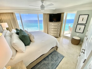 Quarto com uma cama grande, ventilador de teto, televisão, cômoda e vista para o oceano.