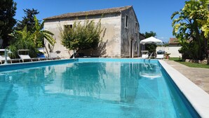 Piscina con sillones de descanso y un edificio al fondo.