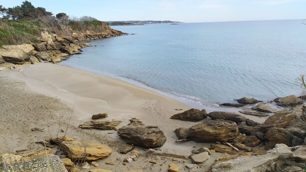 Una playa costera con terreno rocoso y una vista despejada del mar.