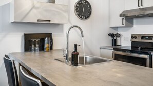 A modern kitchen with a stainless steel sink, a built-in oven, and a clock on the wall.