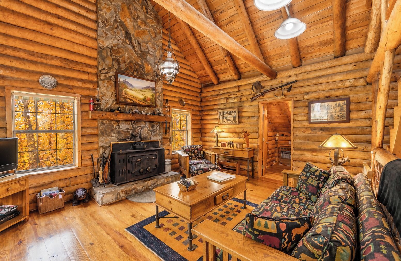 A log cabin interior with a stone fireplace, wooden furniture, and a cozy living area.