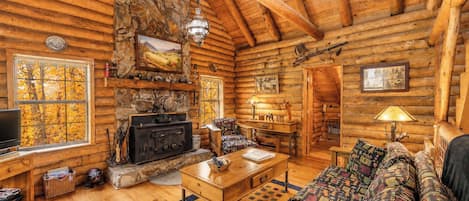 A log cabin interior with a stone fireplace, wooden furniture, and a cozy living area.