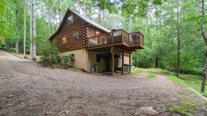 A log cabin with a porch and a deck, surrounded by a forest. - 3BR cottage on the Toccoa River; fish from the yard, stargaze at the firepit! (Suches)