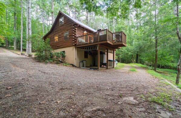Une cabane en rondins dotée d’un porche et d’une terrasse, entourée d’une forêt.