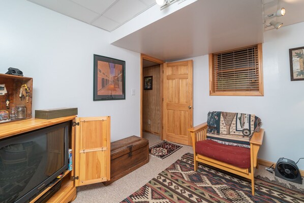 A cozy living room with a wooden cabinet, a television, a patterned armchair, and a door leading to another room.
