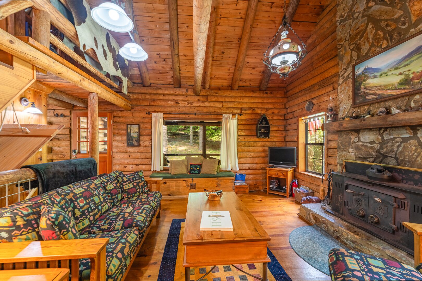 Un intérieur de chalet chaleureux, avec un revêtement mural en bois, une cheminée, un canapé, une table et un téléviseur.