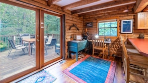 A cabin interior with a dining area, a desk, and a large window overlooking a forest. - 3BR cottage on the Toccoa River; fish from the yard, stargaze at the firepit! (Suches)