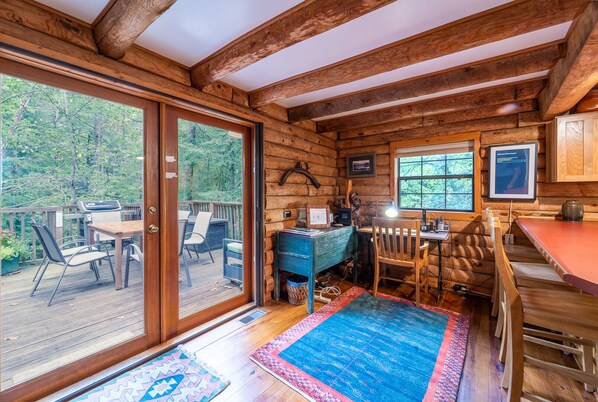 L’intérieur d’une cabane comprend un coin repas, un bureau et une grande fenêtre donnant sur une forêt.