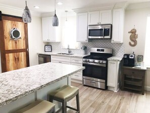 A modern kitchen with white cabinetry, a central island, stainless steel appliances, and pendant lighting.