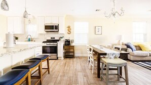 Une cuisine moderne avec des meubles blancs, un îlot central doté de tabourets, un coin repas avec une table et des chaises, et un lustre.