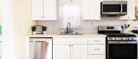 A modern kitchen with white cabinets, stainless steel appliances, and a patterned backsplash.