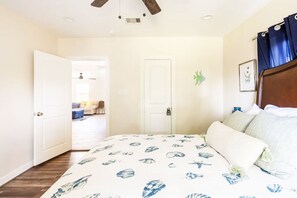 A bedroom with a bed featuring a nautical-themed bedspread, a wooden headboard, and a ceiling fan.