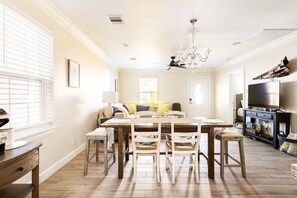 A dining area with a wooden table and chairs, a chandelier, and a sofa in the background.
