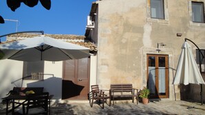 Un bâtiment avec un toit en tuiles, une porte en bois et une fenêtre. On y trouve une table avec des chaises et une plante en pot.