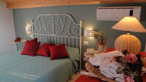 Une chambre à coucher avec un lit, des oreillers rouges, une table de chevet avec une lampe, un panier rempli de serviettes et un vase de fleurs.
