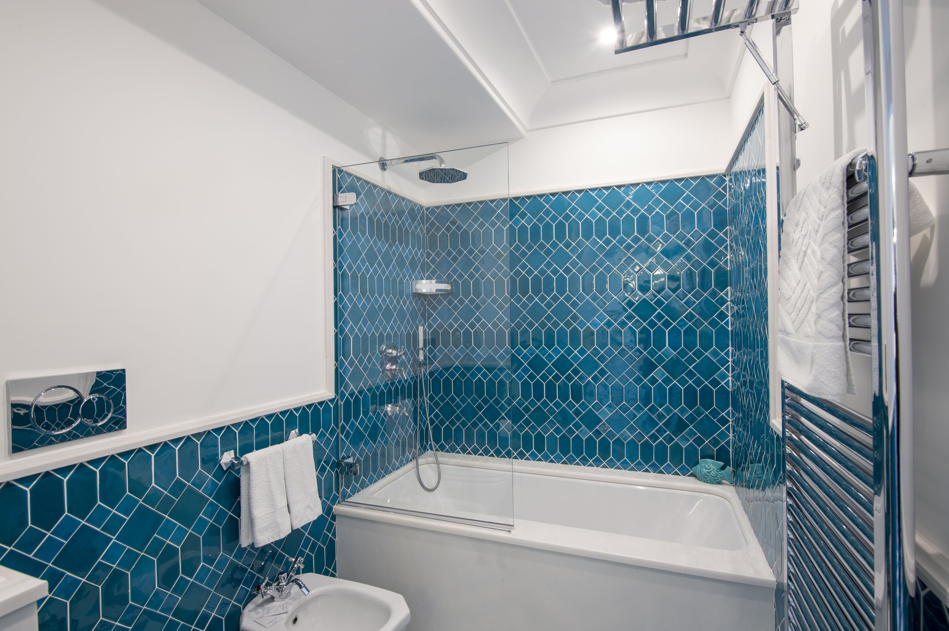 A modern bathroom with a glass-enclosed shower, a white bathtub, and a blue-tiled wall.