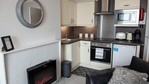 A modern kitchen with a built-in oven, microwave, and stainless steel appliances. There is a small trash bin and a framed welcome sign on the wall. - Highcliffe Promenade Suite (Cleveleys)