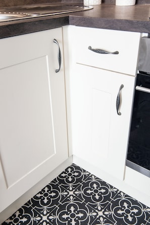 A kitchen with white cabinets, black countertops, and patterned floor tiles. - Highcliffe Promenade Suite (Cleveleys)