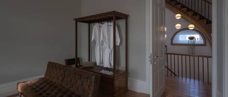A bedroom with a wooden four-poster bed, a brown tufted sofa, and a large mirror. A staircase with wooden railings and a view of the outside is visible through an arched window.