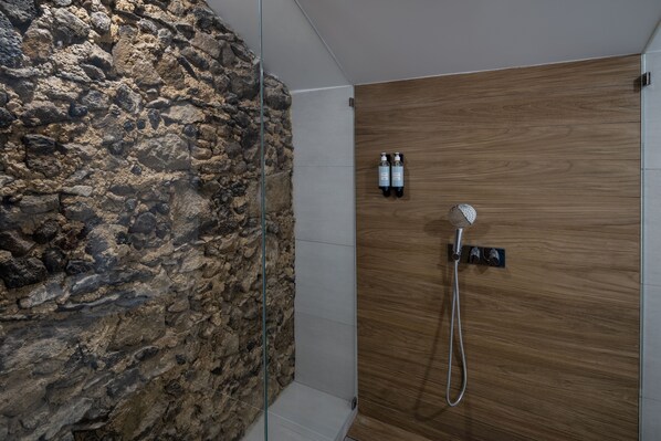 A shower with a wooden panel wall, a glass enclosure, and two bottles of shampoo. - Casa do Páteo - Charming House (Ponta Delgada)