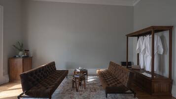 Uma sala de estar com dois sofás marrons, uma mesa de centro de madeira, uma mesinha lateral e um guarda-roupa espelhado com roupas penduradas.