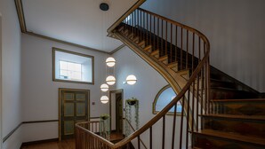 Uma escada de madeira com guarda-corpo de vidro, uma porta com janela e luminárias pendentes.