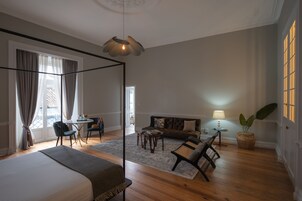 Un dormitorio espacioso con una cama grande, una zona de estar con sofá y sillones, una mesa de comedor y vistas al exterior a través de un ventanal.