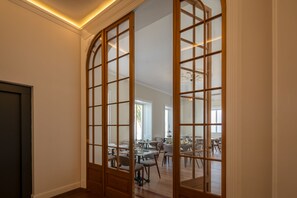 A room with a wooden partition with glass panels, a dining area with tables and chairs, and a view of a kitchen in the background. - Casa do Páteo - Charming House (Ponta Delgada)