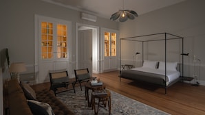 Quarto com cama de dossel, sofá, duas cadeiras, mesa pequena e tapete estampado.