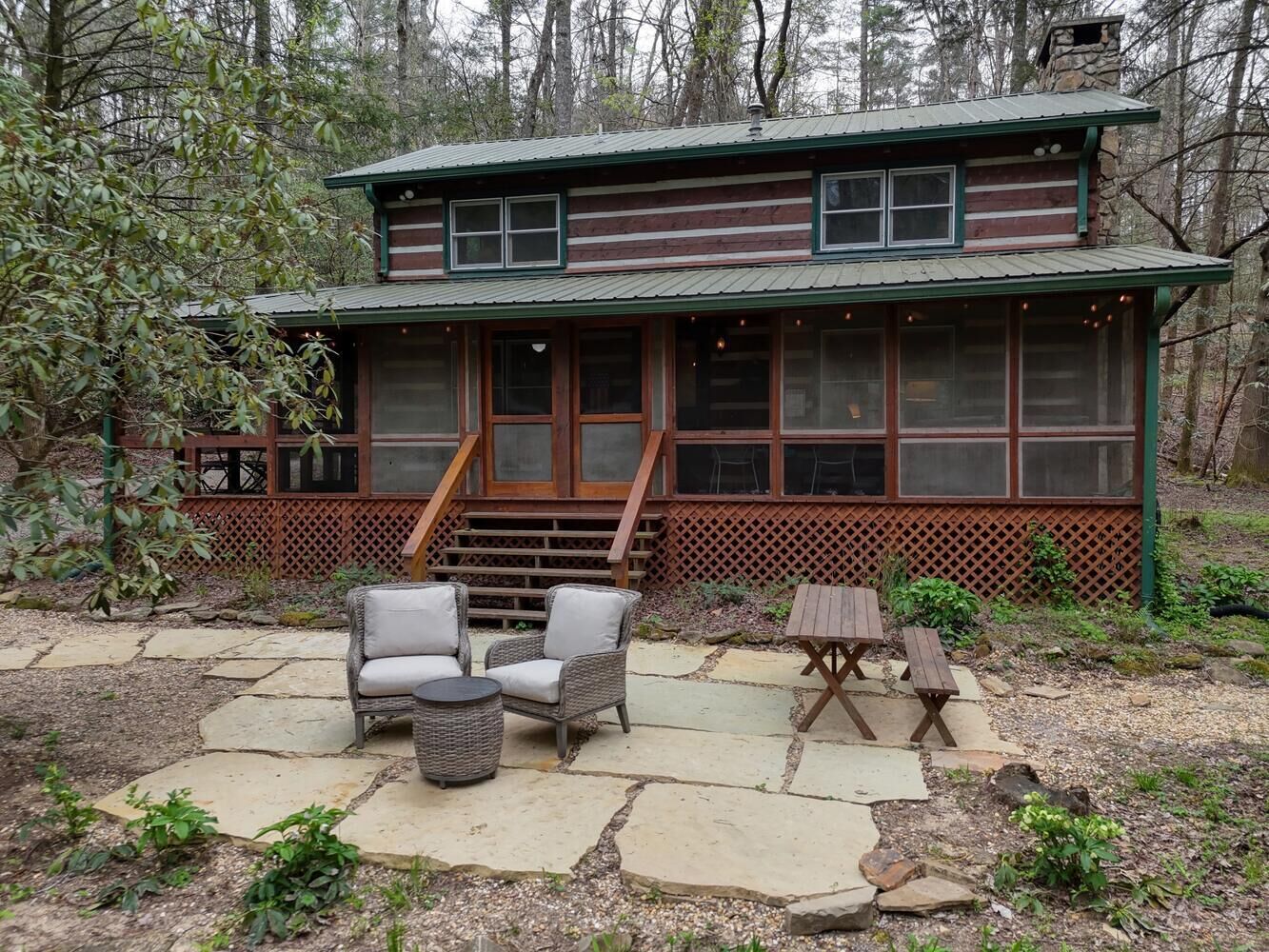 Un chalet rustique doté d’un patio en pierre, de meubles en osier et d’une table en bois.