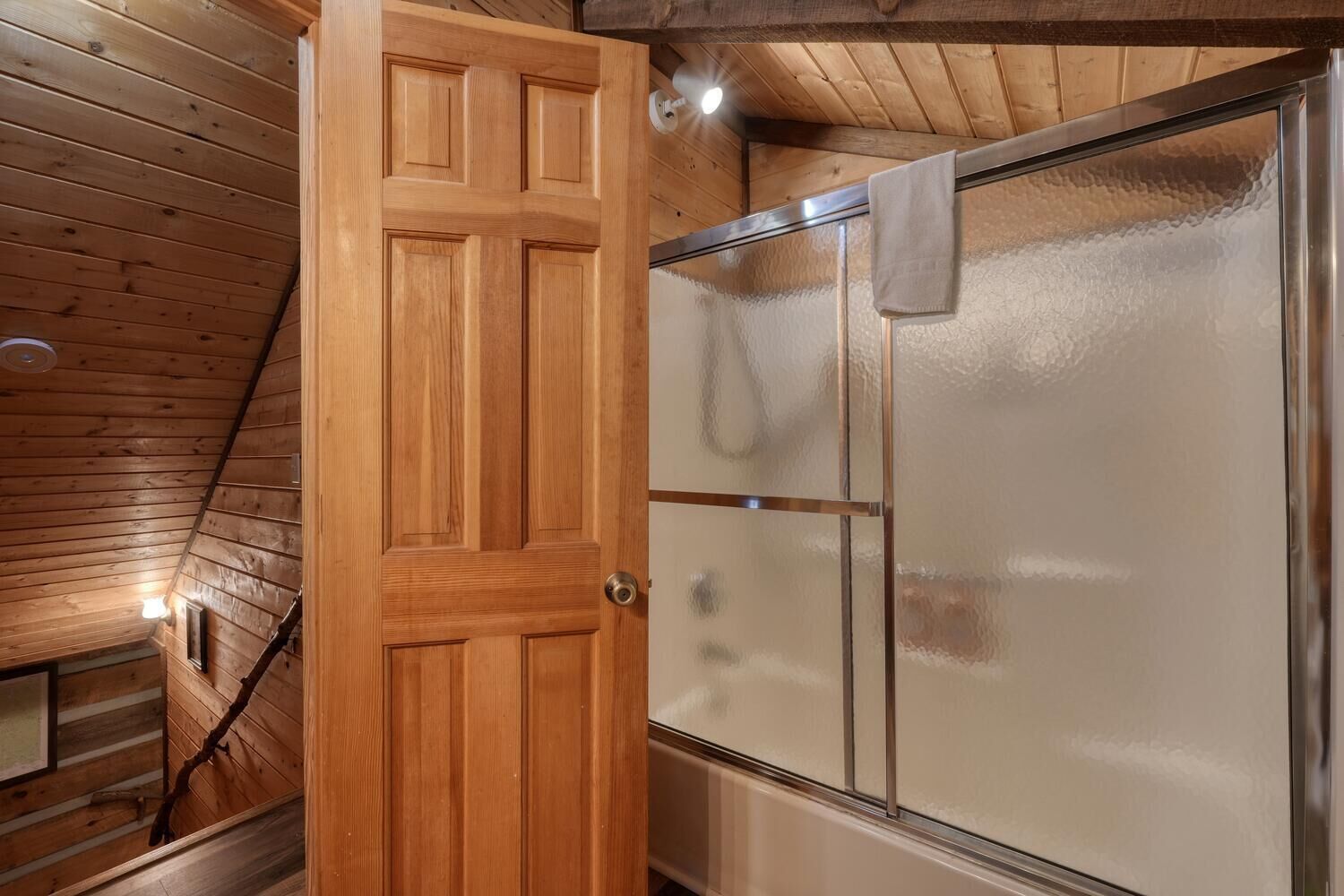 A wooden door leading to a room with a glass shower enclosure.