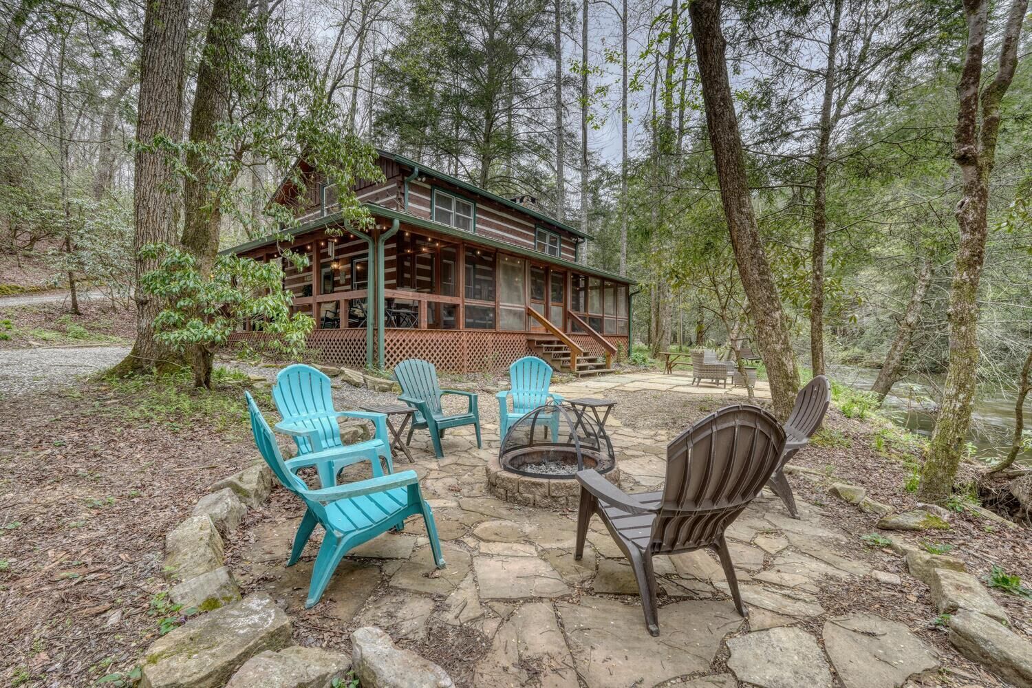 A cabin with a stone patio, outdoor seating, and a forest backdrop.