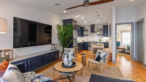 Una sala de estar moderna con un televisor grande, muebles oscuros, una mesa redonda y un ventilador de techo.
