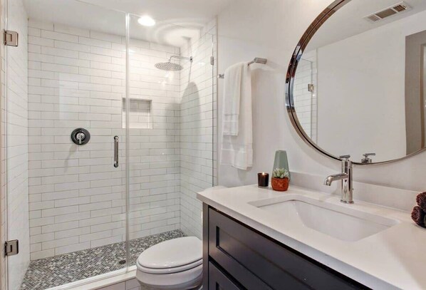 A modern bathroom with a glass-enclosed shower, a white sink, and a round mirror.