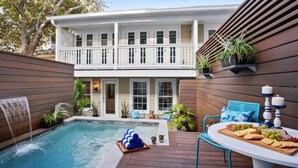 Un área de piscina con un jacuzzi, una terraza de madera, y una mesa con aperitivos y velas.