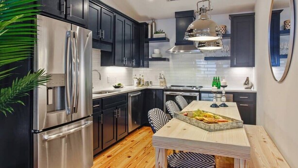Una cocina moderna con armarios oscuros, electrodomésticos de acero inoxidable y una mesa de comedor de madera.