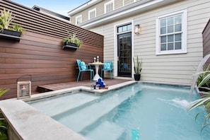 A backyard with a swimming pool, wooden deck, and a small table with chairs.