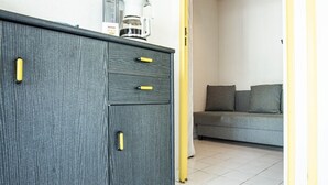 Quarto com guarda-roupa de madeira escura com puxadores amarelos, sofá cinzento com almofadas e máquina de café sobre o guarda-roupa.