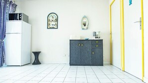 Uma cozinha pequena com geladeira branca, armário de madeira escura, uma mesa e um espelho fixado na parede.