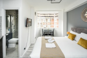 A hotel room with a bed, a window with a view, a bathroom, and a desk. - NEW Sleek & Modern Studio in the Heart of Chelsea (London)