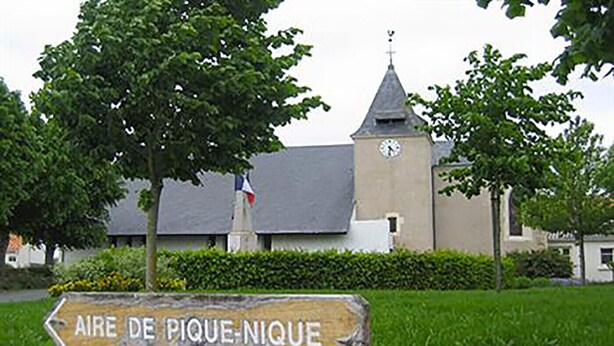 A church with a clock tower and a sign pointing to 'Aire de Pique-Nique'.