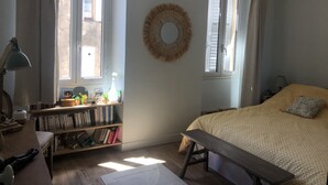 Un dormitorio con cama, estantería, escritorio y ventana con cortinas.