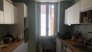 Cocina pequeña con armarios blancos, una ventana, un cubo de basura y un lavamanos.